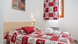 En pænt redt seng med et rødt og hvidt tæppe, en rød pude og en lampe på sengebordet.