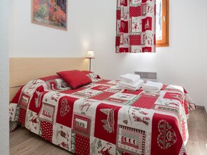 A neatly made bed with a red and white quilt, a red pillow, and a lamp on the bedside table. - Apartment in Valmeinier with Valley Views (Valmeinier)