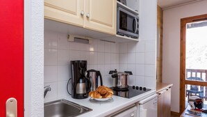 Et lille køkken med mikroovn, kaffemaskine og croissanter på bordet.