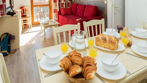 En morgenmadsopsætning med croissanter, appelsinjuice og et rundstykke på et bord med hvide tallerkener og kopper.