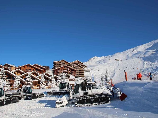 A snow-covered ski resort with wooden chalets and a snow grooming machine.