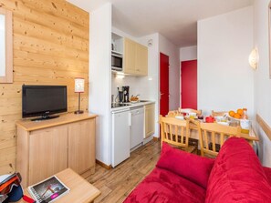 A compact living space with a kitchenette, a dining area, a television on a wooden stand, and a red sofa.