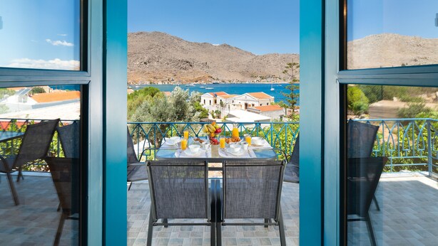 A balcony with a table set for two, overlooking a coastal town with mountains in the background. - Royal Villa Pedi - Symi (Symi)