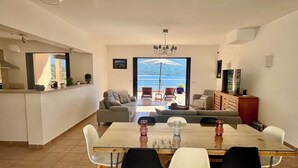 A modern living room with a sofa, a dining table with chairs, a TV, and a view of the sea through a large window. - Beautiful house. Wonderful sea view (Casaglione)