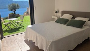 A bedroom with a bed, pillows, a nightstand, and a view of a lake and mountains. - Beautiful house. Wonderful sea view (Casaglione)