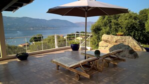 A balcony with a view of the sea, a lounge chair, an umbrella, and potted plants. - Beautiful house. Wonderful sea view (Casaglione)