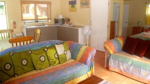 Una habitación acogedora con kitchenette, dos sofás coloridos, una mesa de comedor y un ventilador.