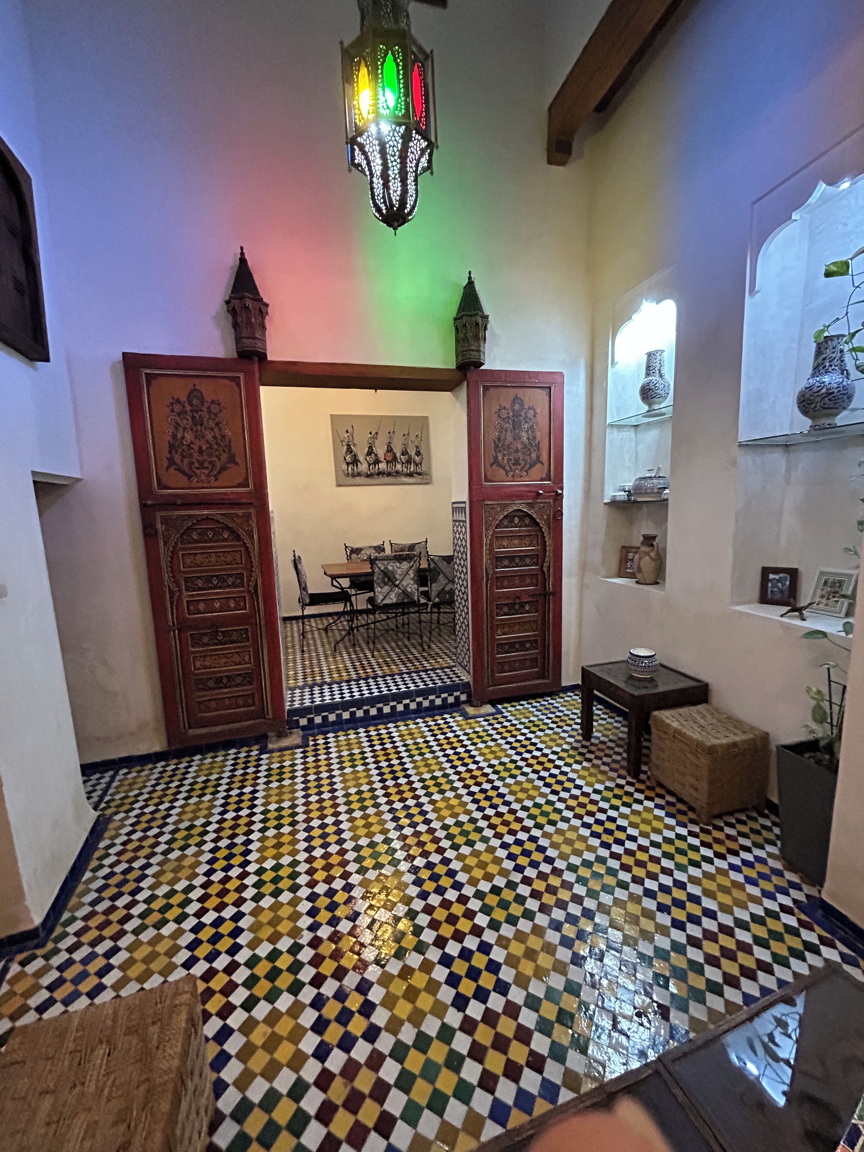 Um quarto com piso xadrez, um lustre e uma porta com desenhos elaborados.