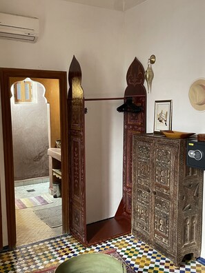 Une pièce avec un sol à carreaux, un buffet en bois orné de sculptures complexes, une lampe suspendue et un tableau encadré au mur.