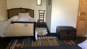 A bedroom with a bed, a chair, a wooden chest, and a patterned rug. - Spacious House,  Cosy Accommodation. Log stove. Countryside forest river walks. (La Grée-Saint-Laurent)