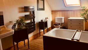 A bathroom with a bathtub, wooden floor, a toilet, a sink, a small table with a plant, and a framed picture on the wall. - Spacious House,  Cosy Accommodation. Log stove. Countryside forest river walks. (La Grée-Saint-Laurent)