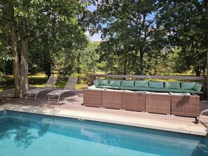 Un espace aménagé au bord de la piscine, avec des chaises longues, un canapé en osier doté de coussins et une terrasse en bois.