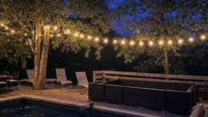 Un espace extérieur avec une piscine, des chaises longues, une terrasse en bois et des guirlandes lumineuses.