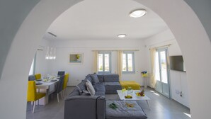 A modern living room with a dining area, grey sofas, yellow chairs, and a white coffee table with fruit. - 3 bedroom Luxury villa , 200m by  famous Monolithos  beach!  (Έξω Γιαλός Καρτεραδου)