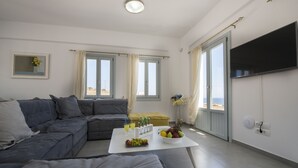 A modern living room with a grey sectional sofa, a white coffee table with fruits and drinks, and a TV on the wall. - 3 bedroom Luxury villa , 200m by  famous Monolithos  beach!  (Έξω Γιαλός Καρτεραδου)