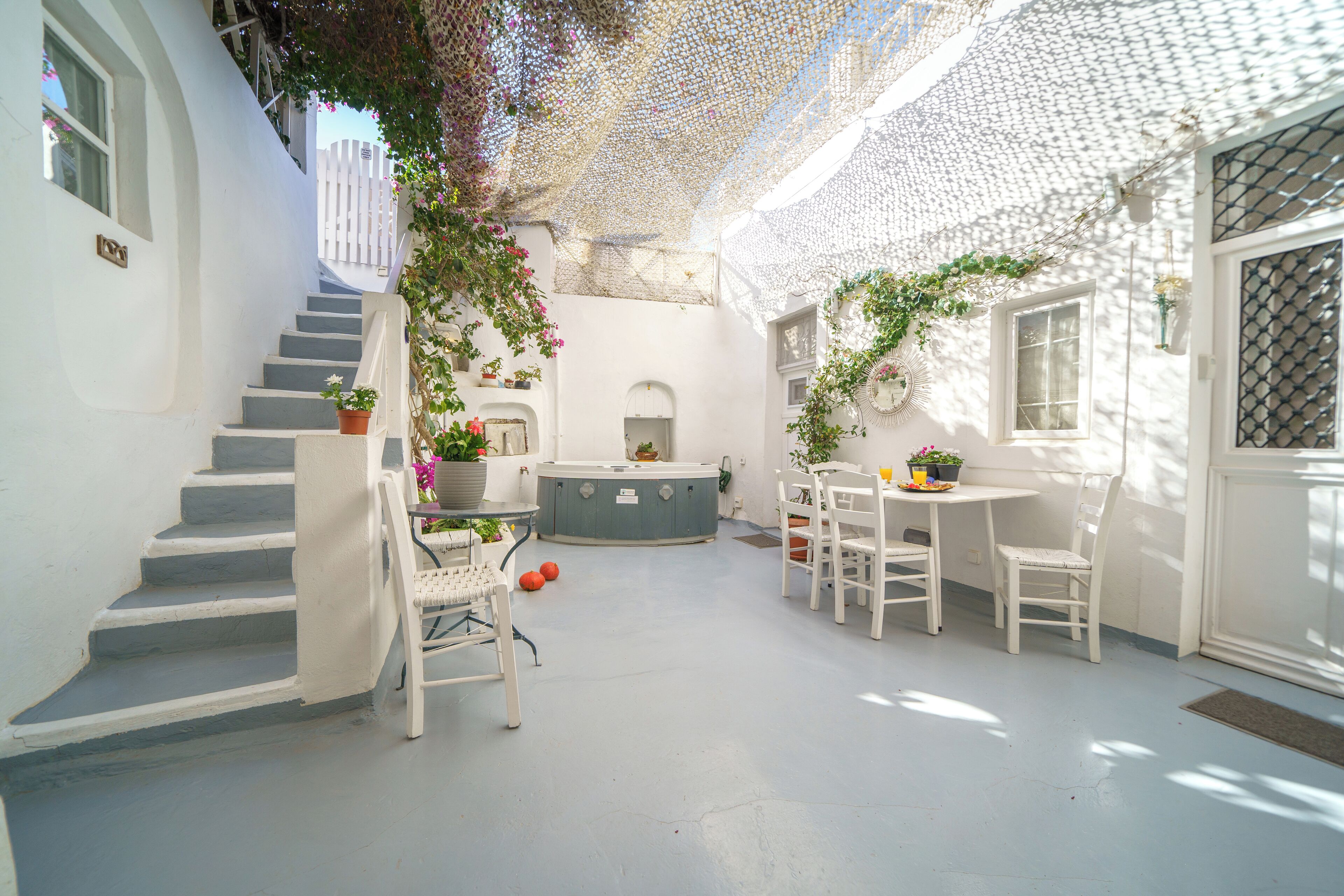 Un cortile dalle pareti bianche con una scalinata, un angolo relax con sedie e un tavolo, e una piccola fontana.