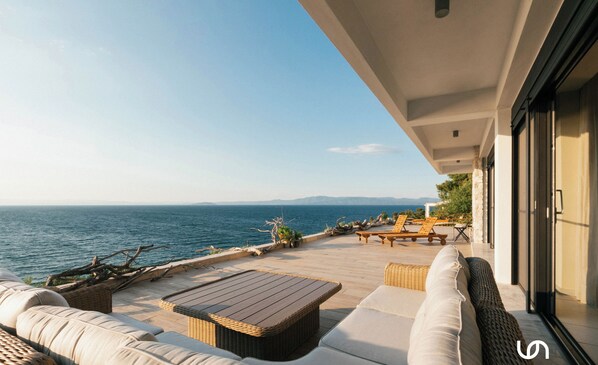 A terrace with wicker furniture, a wooden table, and a view of the sea.