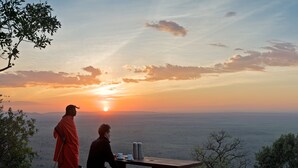 Two people sitting at a wooden bench overlooking a vast landscape during sunset.