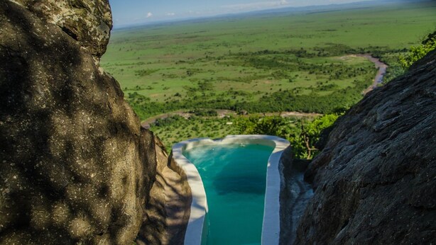 A natural pool carved into a cliffside overlooking a vast green landscape.