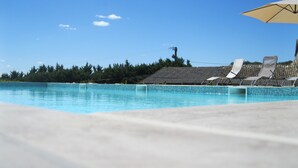 Une piscine d’un bleu éclatant, bordée de carreaux, entourée de chaises longues et d’un parasol.
