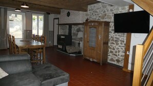 Een gezellige woonkamer met een stenen muur, een open haard, een televisie en een eethoek met houten meubels.