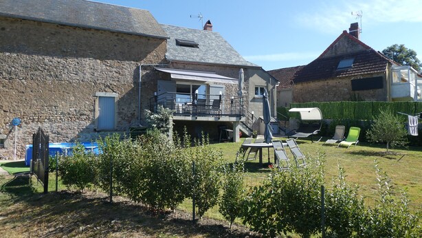 Een stenen gebouw met een balkon, een zwembad en een omheinde tuin met ligbedden.