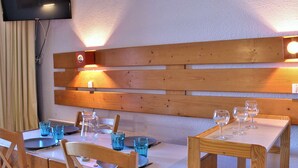 Ein Essbereich mit Holztischen und -stühlen, einem an der Wand montierten Fernseher und einer Holzbank mit integrierter Beleuchtung.