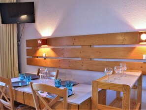 Un comedor con mesas y sillas de madera, un televisor montado en la pared y un banco de madera con iluminación integrada.
