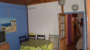 Een kamer met een houten plafond, een eettafel met stoelen, een televisie en een deur naar een andere kamer.