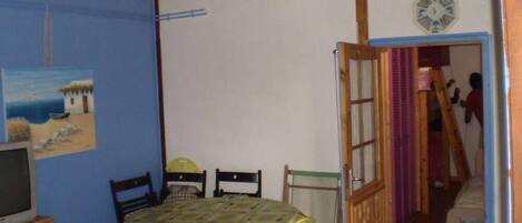 Una habitación con techo de madera, una mesa de comedor con sillas, un televisor y una puerta que da a otra habitación.