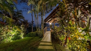 A nighttime pathway leading to a building surrounded by lush tropical vegetation. - Cliff House with Private Infinity Pool. 3 Minute Walk to the Beach. (Puntarenas)