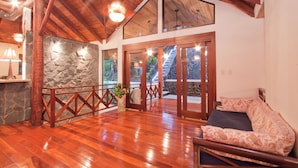 Una habitación amplia con suelo de madera, pared de piedra y balcón con barandilla de madera.