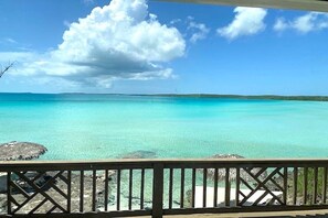 Een helder uitzicht op turquoise water vanaf een houten terras met een leuning.