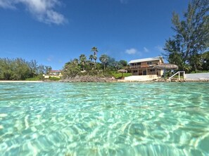 Une propriété située en bord de mer, avec une eau cristalline, une structure à toit de chaume et un grand bâtiment doté de balcons.