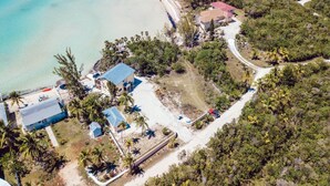 Vue aérienne d’une propriété située sur la côte, comprenant plusieurs bâtiments, une plage et une route.