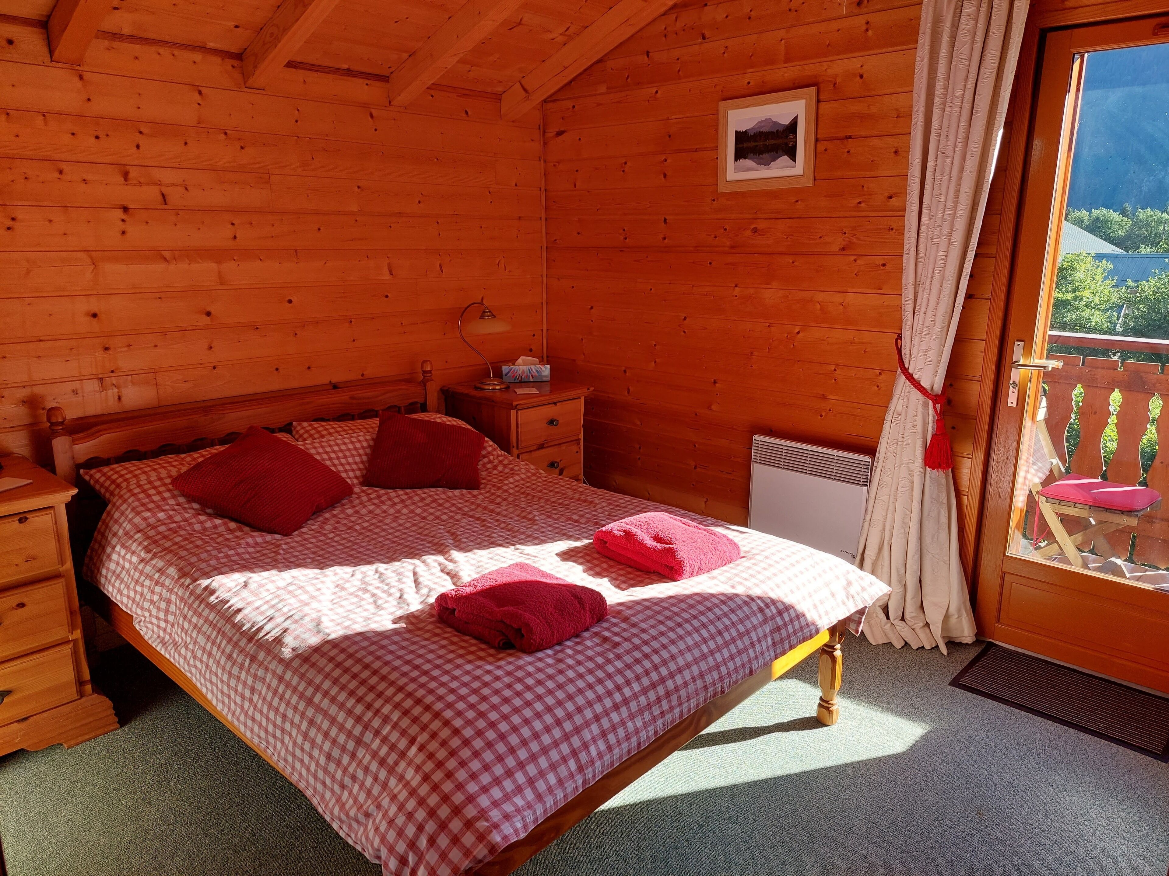 A wooden cabin bedroom with a bed, nightstands, a heater, and a window with curtains.