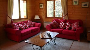 A wooden cabin interior with two red sofas, a chessboard, and a lamp. - Delightful Chalet, village location, garden, parking, views and WiFi (Le Biot)
