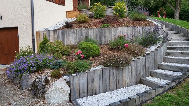 A house with a wooden deck, a stone pathway, and various plants and flowers. - Delightful Chalet, village location, garden, parking, views and WiFi (Le Biot)