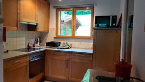 A kitchen with wooden cabinets, a stove, a microwave, and a window with a view of a house. - Delightful Chalet, village location, garden, parking, views and WiFi (Le Biot)