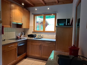 A kitchen with wooden cabinets, a stove, a microwave, and a window with a view of a house.