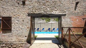 Un bâtiment en pierre doté d’un espace piscine, comprenant des chaises longues bleues et des parasols.