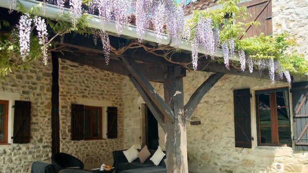 Un bâtiment en pierre doté d’un patio couvert, aménagé avec des meubles en osier et agrémenté d’un arbre.
