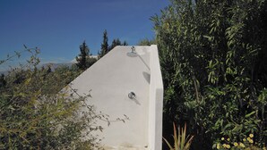 A white outdoor shower with a showerhead, surrounded by greenery and a potted plant. - Apartment 80 m2 for 4 people, sea view, swimming pool, parking, washing machine (Kamilari)