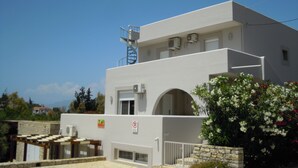 A modern building with a flat roof, a staircase, and a small garden with flowers. - Apartment 80 m2 for 4 people, sea view, swimming pool, parking, washing machine (Kamilari)