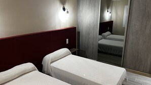 A hotel room with two single beds, a wardrobe with a mirror, and a wall-mounted light fixture.