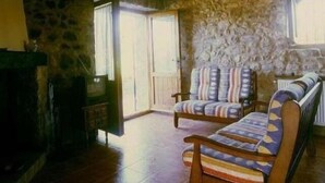 Una habitación con paredes de piedra, piso de madera, dos sillones a rayas, un sofá y una chimenea.