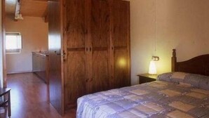 Un dormitorio con un armario de madera, una cama con colcha estampada, una lámpara de noche y una mesita.