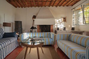 Ein Wohnzimmer mit Kamin, gestreiften Sofas, einem Glastisch und einer rustikalen Decke.
