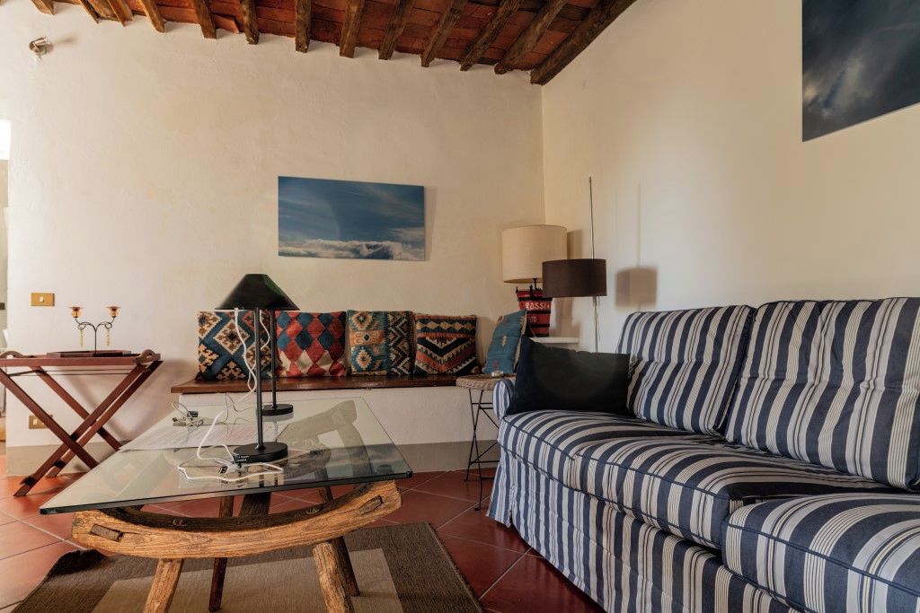 A living room with a glass coffee table, striped sofa, colorful cushions, a lamp, and a painting on the wall.