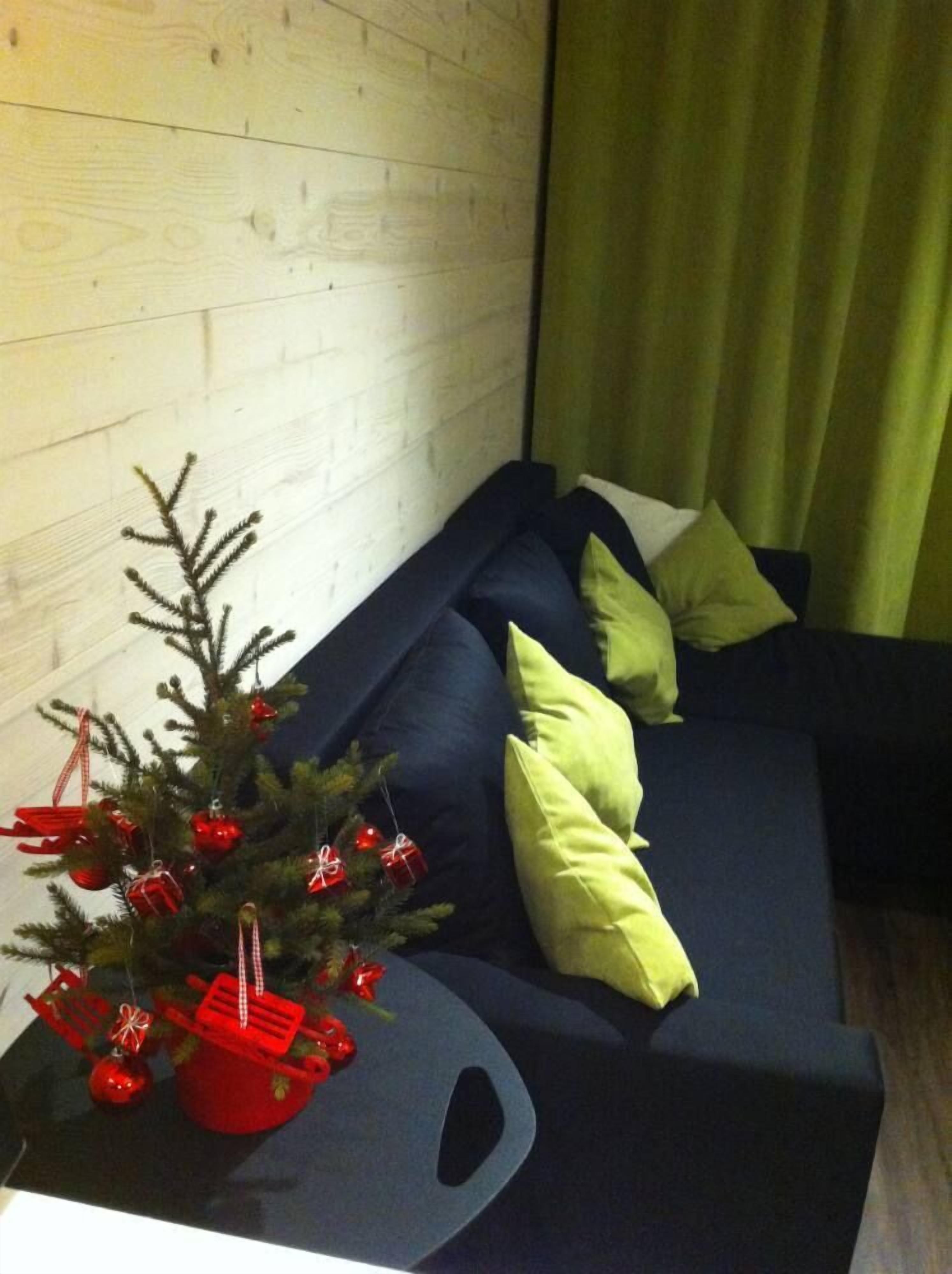 A modern living room with a dark blue sofa, green cushions, and a small Christmas tree with red ornaments on a wooden table.